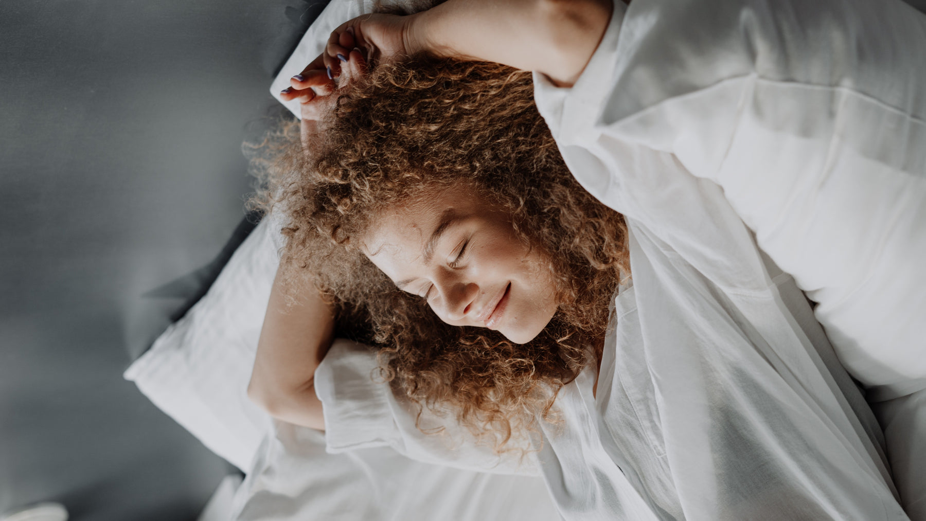 Woman with curly hair in a white top laying back on a body pillow and smiling