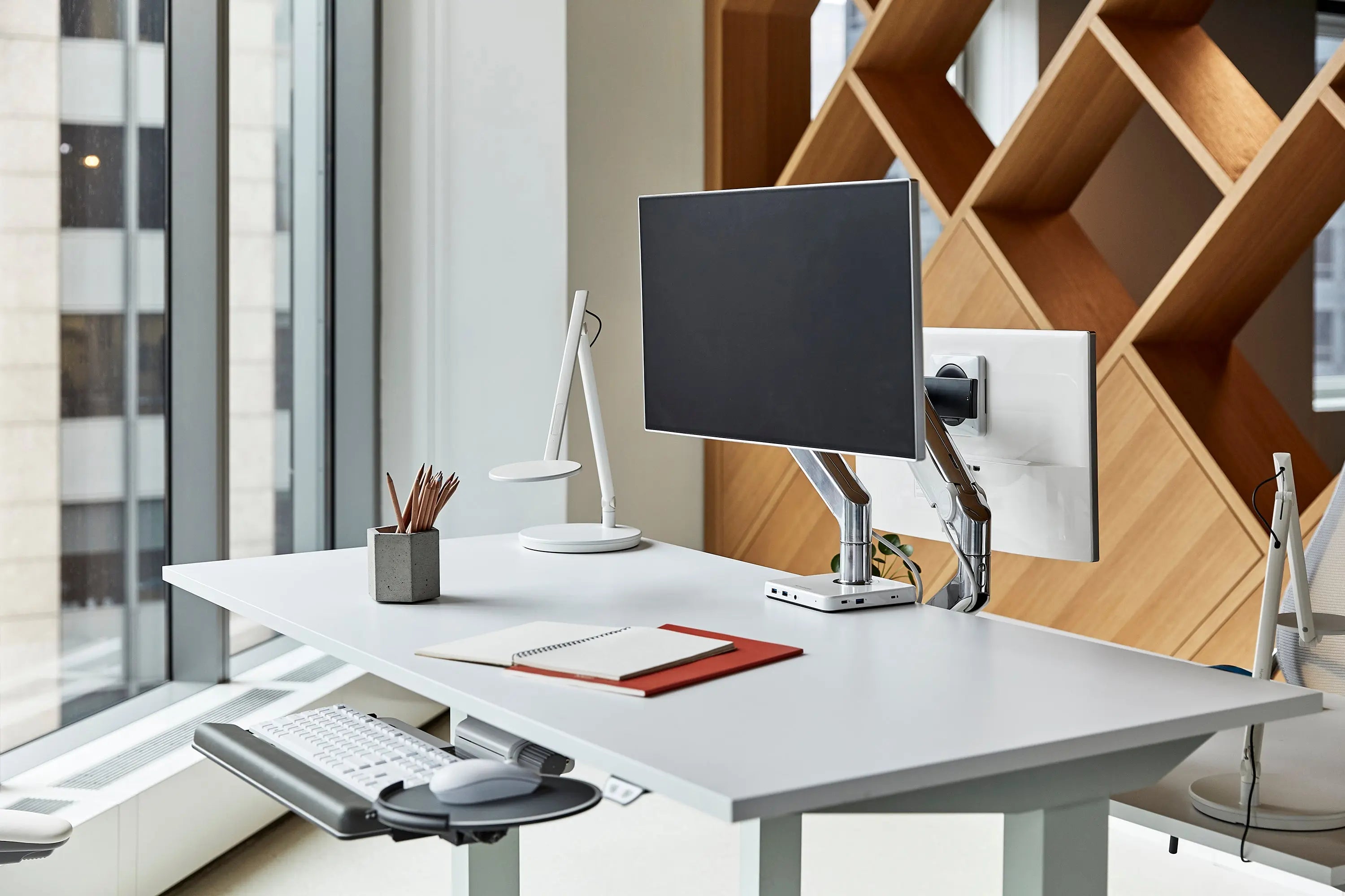 Standing desk in an office setting with keyboard tray and a monitor.