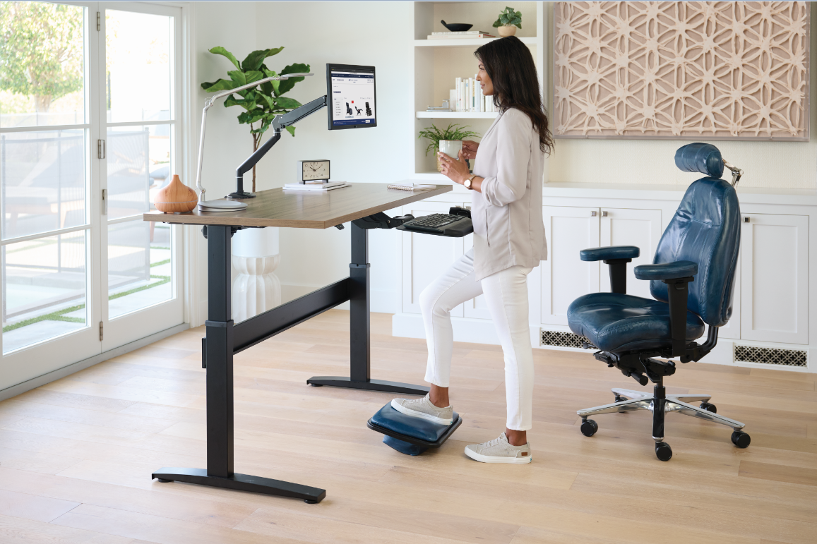 Ergonomic office furniture homepage image featuring a Lifeform Ultimate Executive Office Chair, an upholstered footrest and a standing desk with a Humanscale monitor arm.