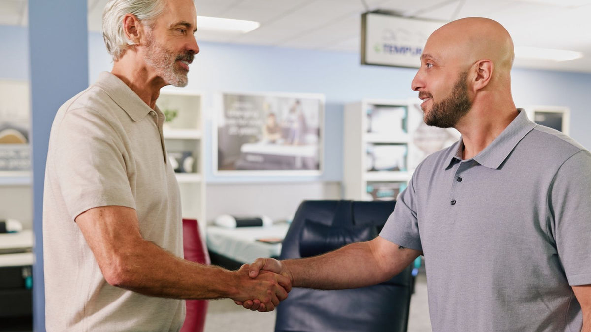 Relax The Back team member shaking hands with a customer inside a wellness and ergonomic furniture showroom.