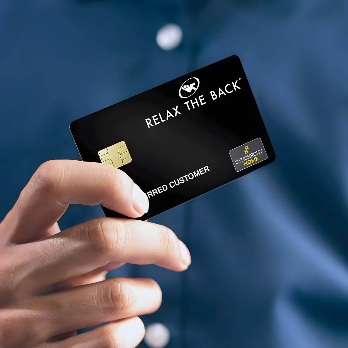 A hand holding a black Relax the Back credit card with a gold chip, set against a blurred blue shirt background.