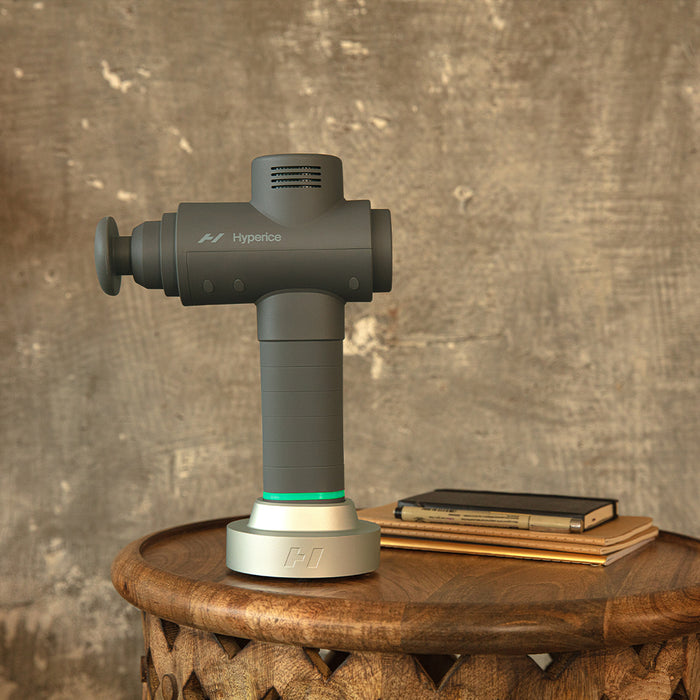Side view of the Hypervolt 2 Handheld Massager with Bluetooth by Hyperice® on a wooden table.