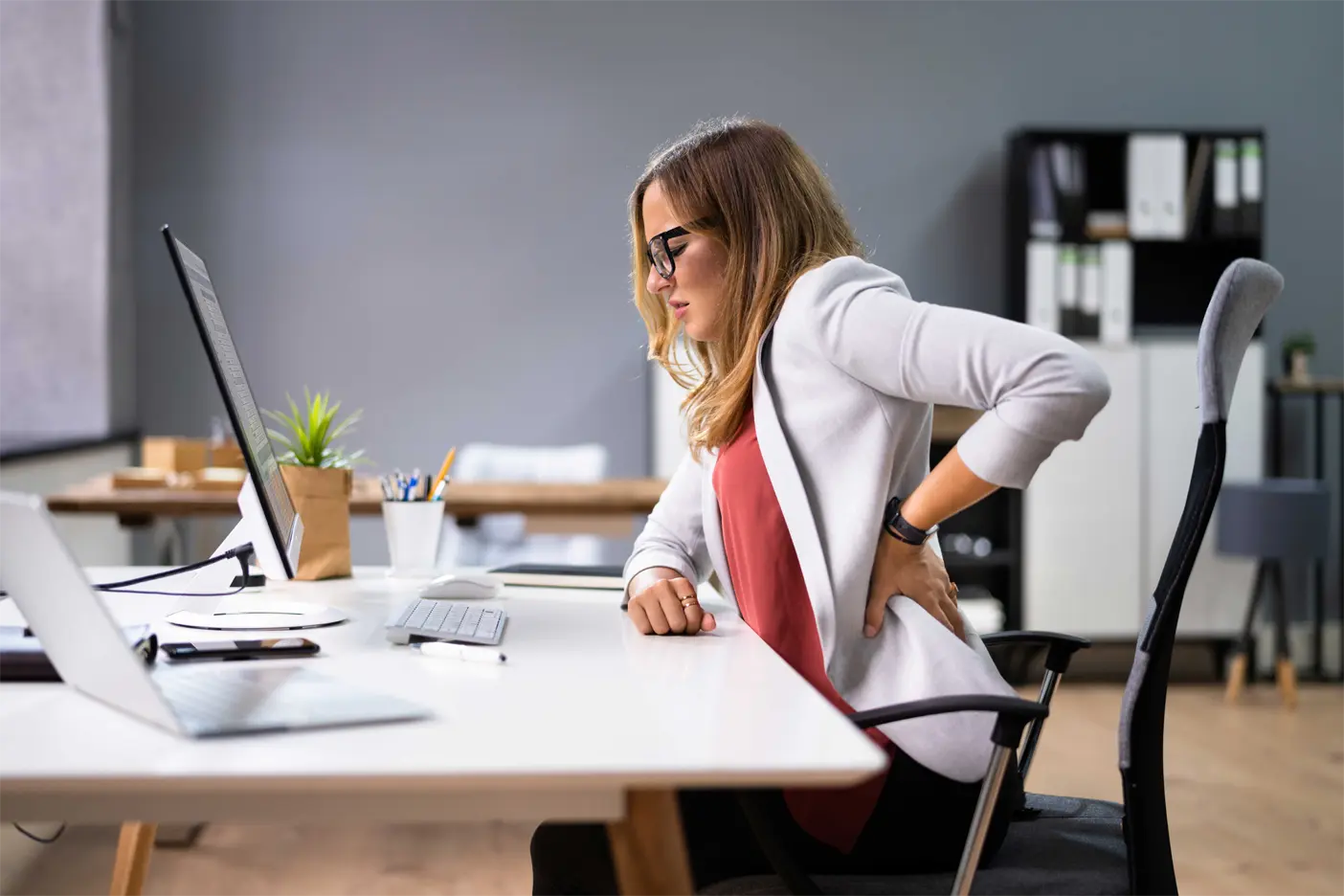 Lady sitting at her desk holding her back