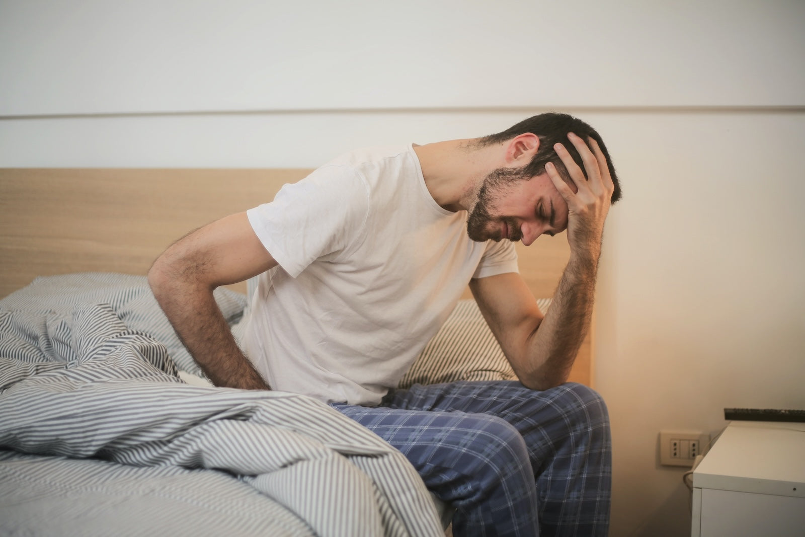 Man sitting on a bed with his head in his hands, appearing distressed.