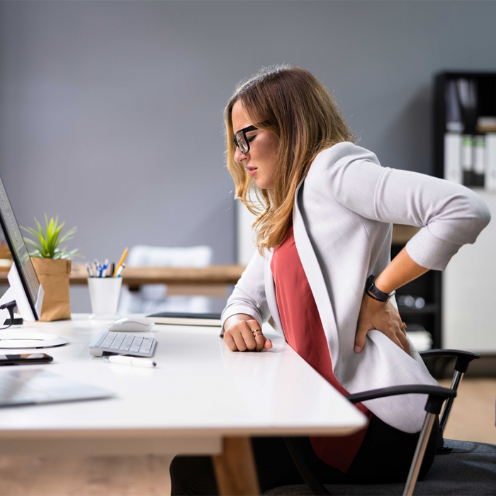 Lady sitting at her desk holding her back