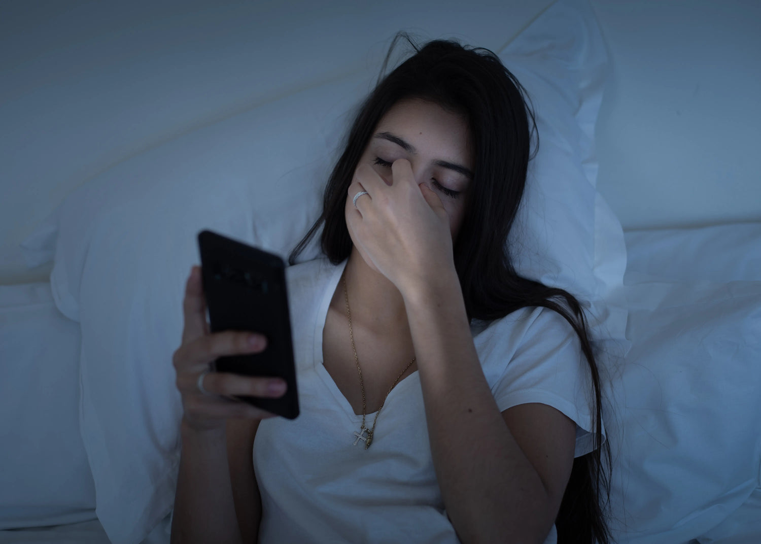 Sleepy girl using mobile phone in bed at night. 