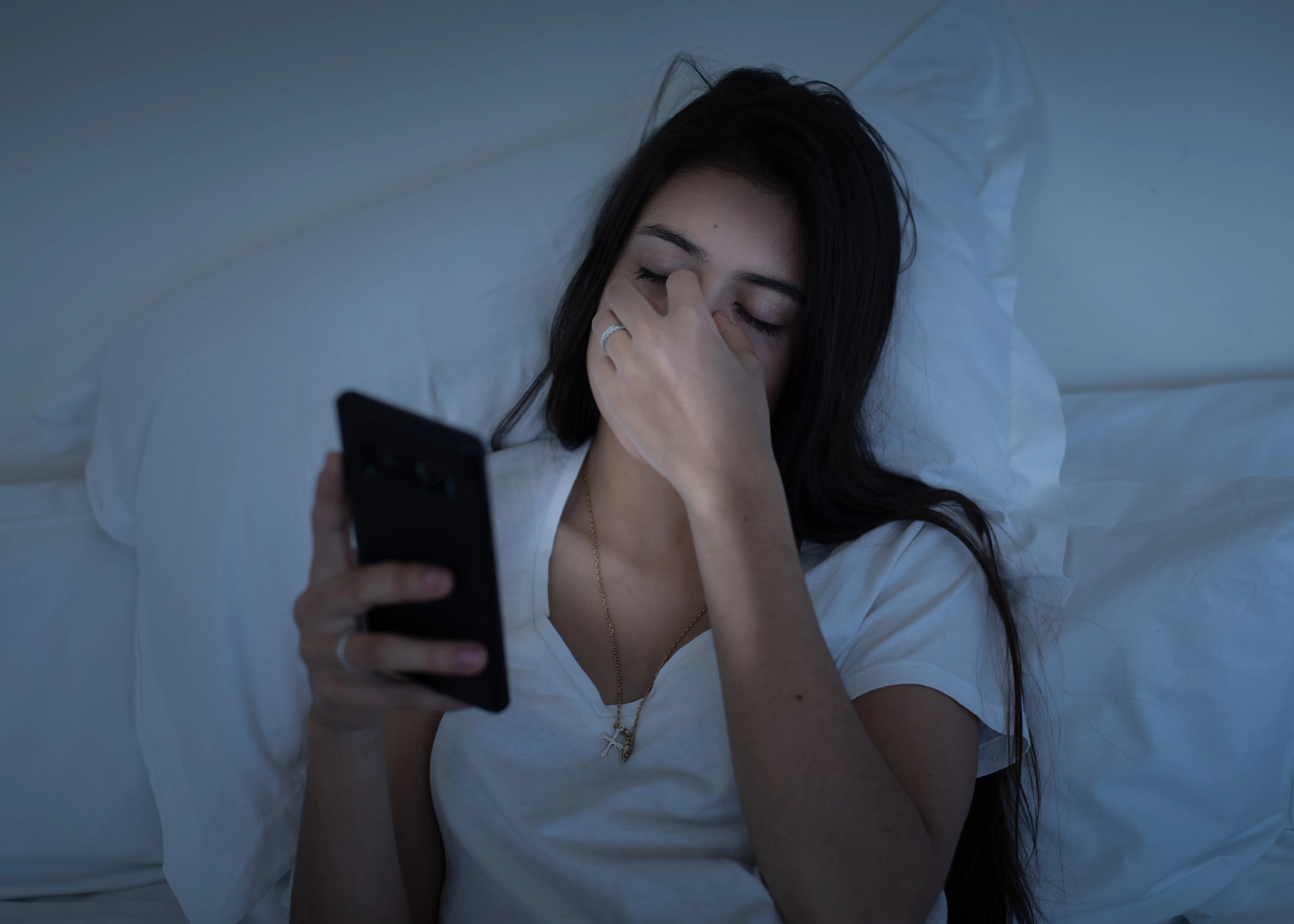 Sleepy girl using mobile phone in bed at night. 