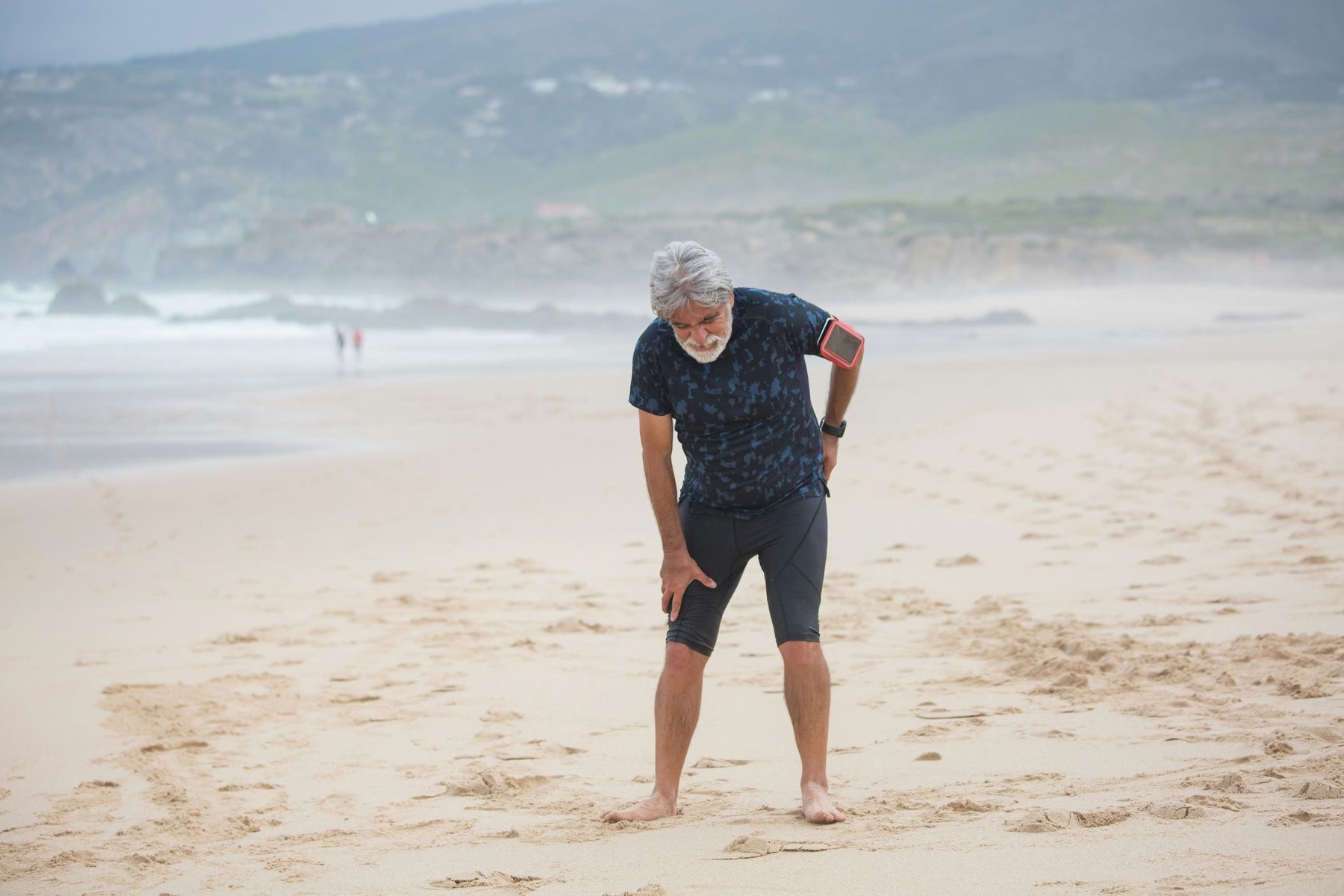 Man bent over holding his sciatica walking on the beach