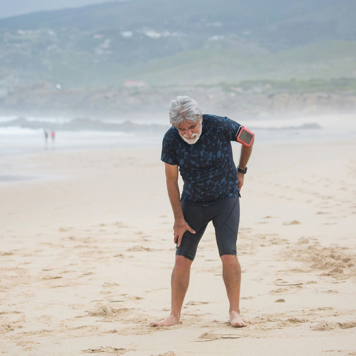 Man bent over holding his sciatica walking on the beach