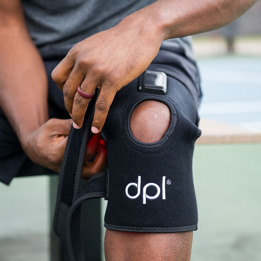 Person wearing a black knee brace with 'dpl' logo on a blurred background
