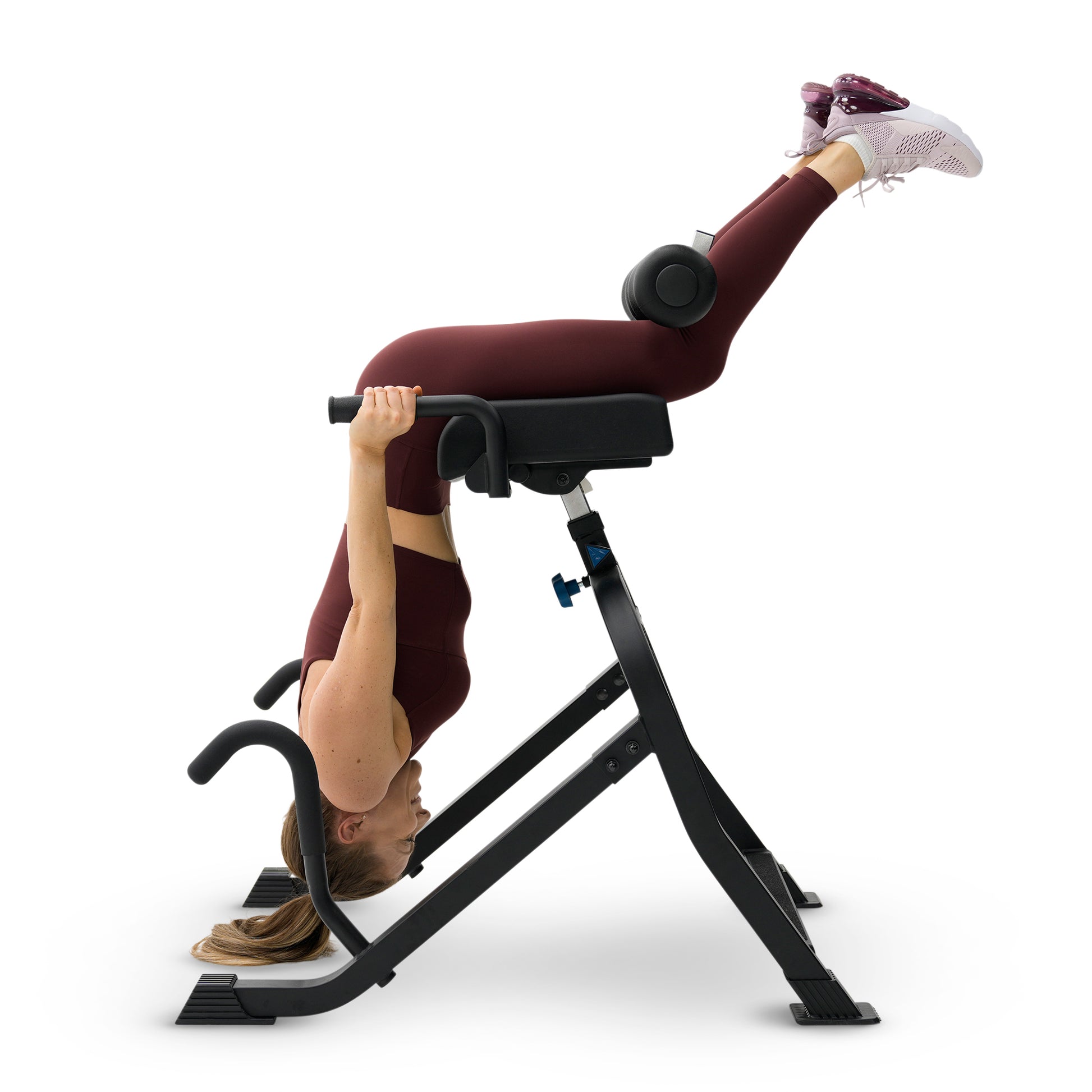 A woman in a maroon athletic outfit performs a leg extension exercise using a black leg press machine on a solid white background.