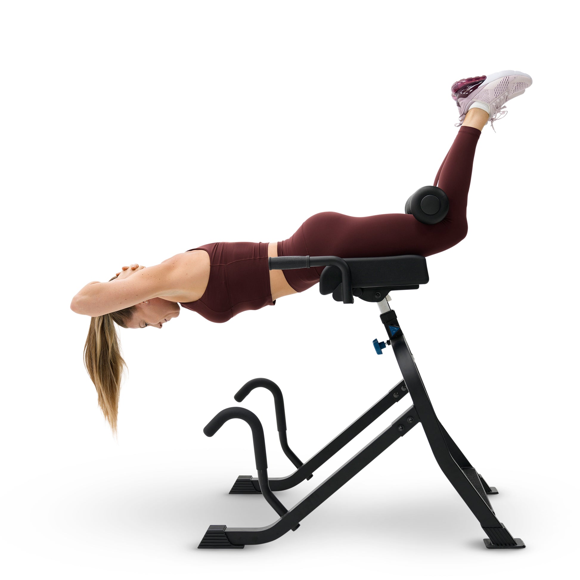A woman in a maroon sports bra and leggings performs a leg exercise on a black DEX II Commercial Inversion & Core Training System isolated on a white background.
