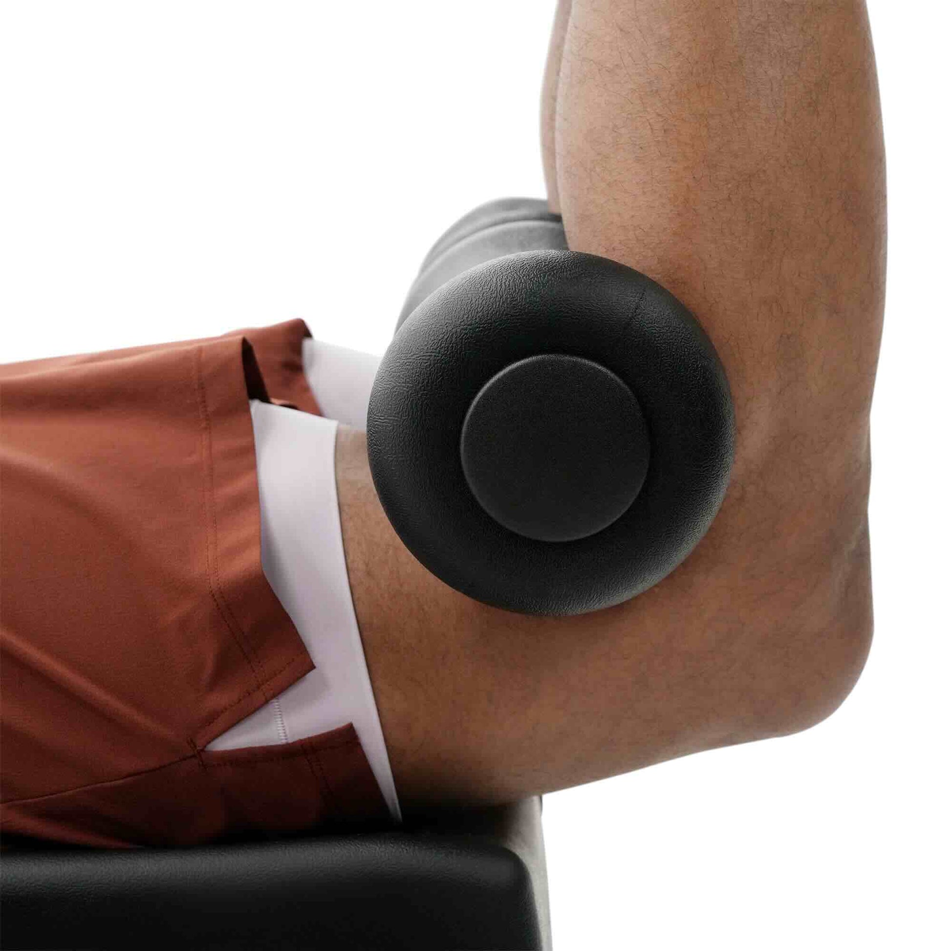 Close-up of a person's bent arm resting on a black padded support, wearing rust-brown shorts and a white shirt, against a white background.