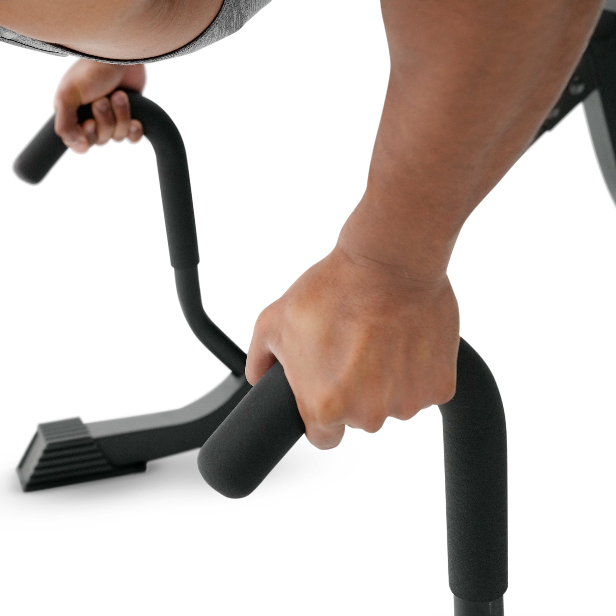 Close-up of a person's hands gripping the foam handles of a black exercise machine on a white background.