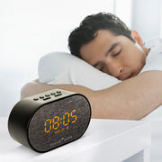 A man sleeping soundly in bed next to a black digital alarm clock with a textured face displaying 00:05 in orange digits.