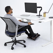 Person using a standing desk with a footrest in a modern office setting