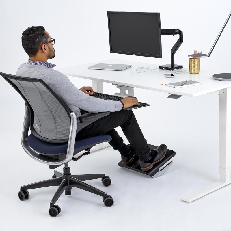 Person using a standing desk with a footrest in a modern office setting