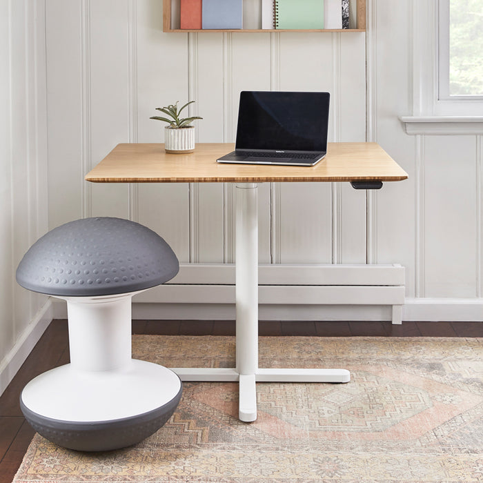 The Ballo Active Stool in front of a bamboo and white base standing desk. 
