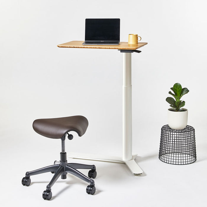 Float Mini Desk show with the Freedom saddle stool next to a wire plant stand with a plant on top.