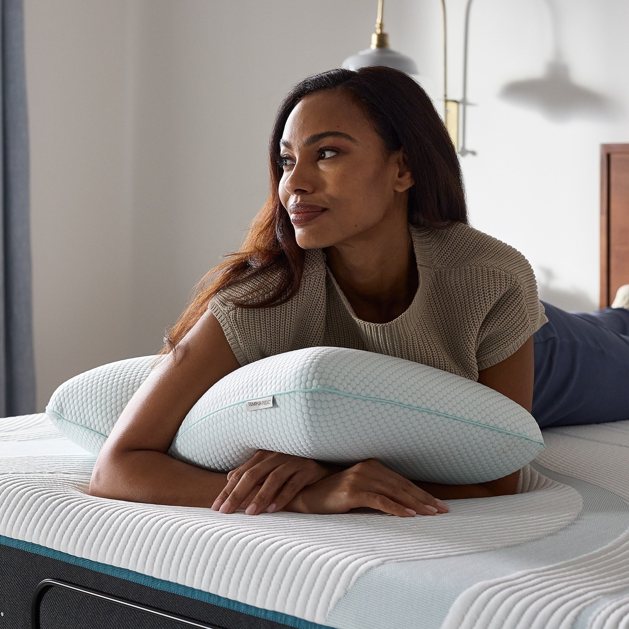 Woman lying on a bed with a pillow, smiling in a bedroom setting