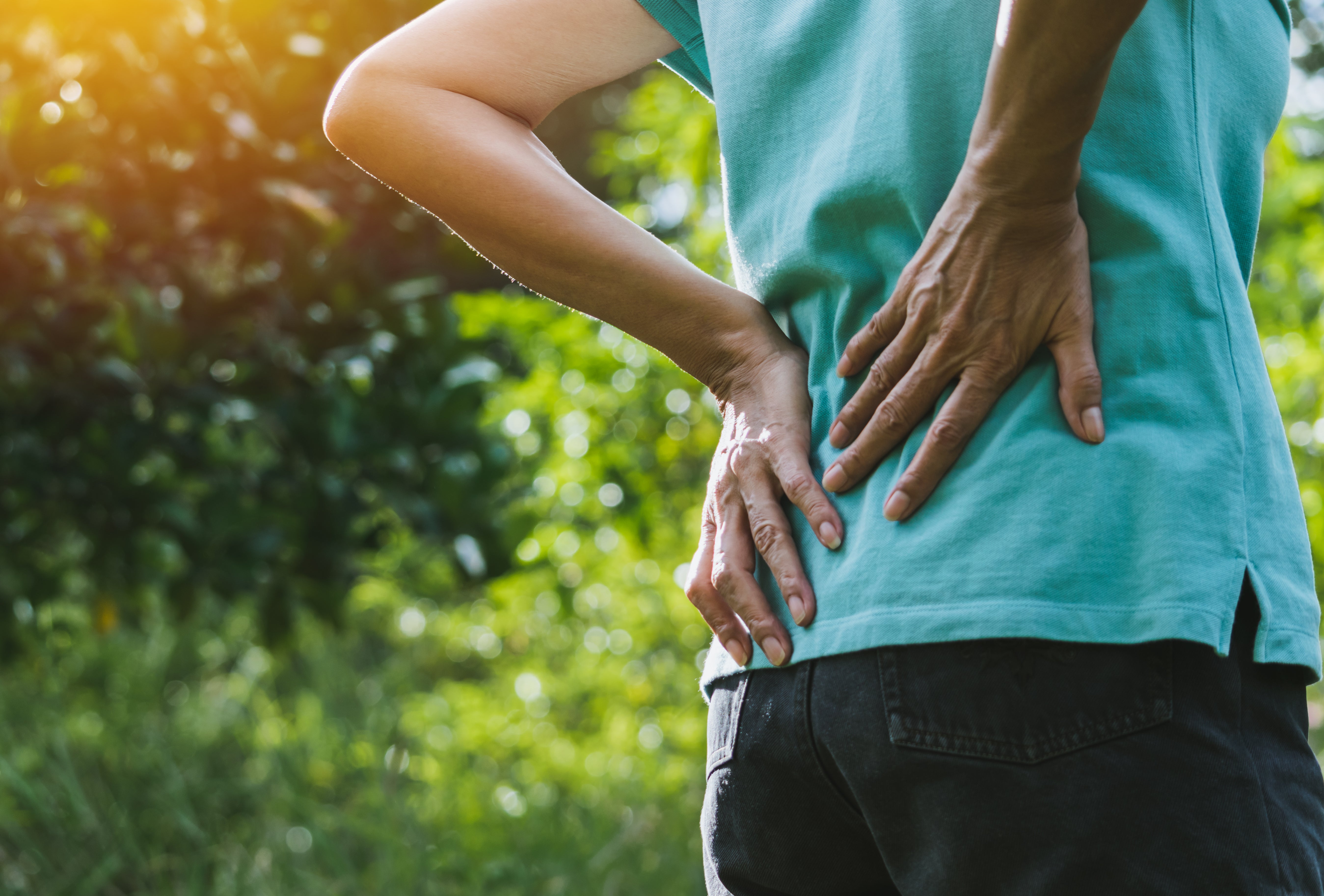 Person holding their lower back in a park setting