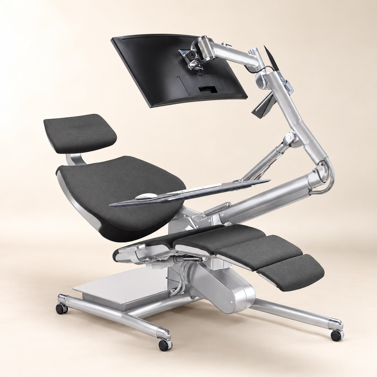 An ergonomic office chair with a silver metal frame and black padded seat, headrest, footrest, and adjustable monitor arm, shown on a light beige studio background.