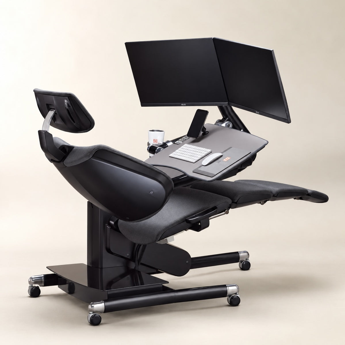 Altwork Workstation in black and gray with reclining ergonomic seat, dual monitors, adjustable desk, keyboard, mouse, and leg support.
