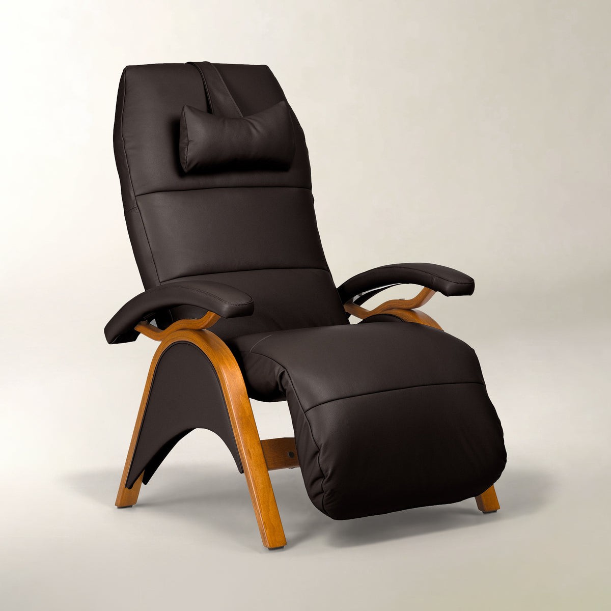 A modern high-back recliner chair with dark brown faux leather upholstery, a matching headrest pillow, and curved light wood legs, shown on a neutral light gray studio background.