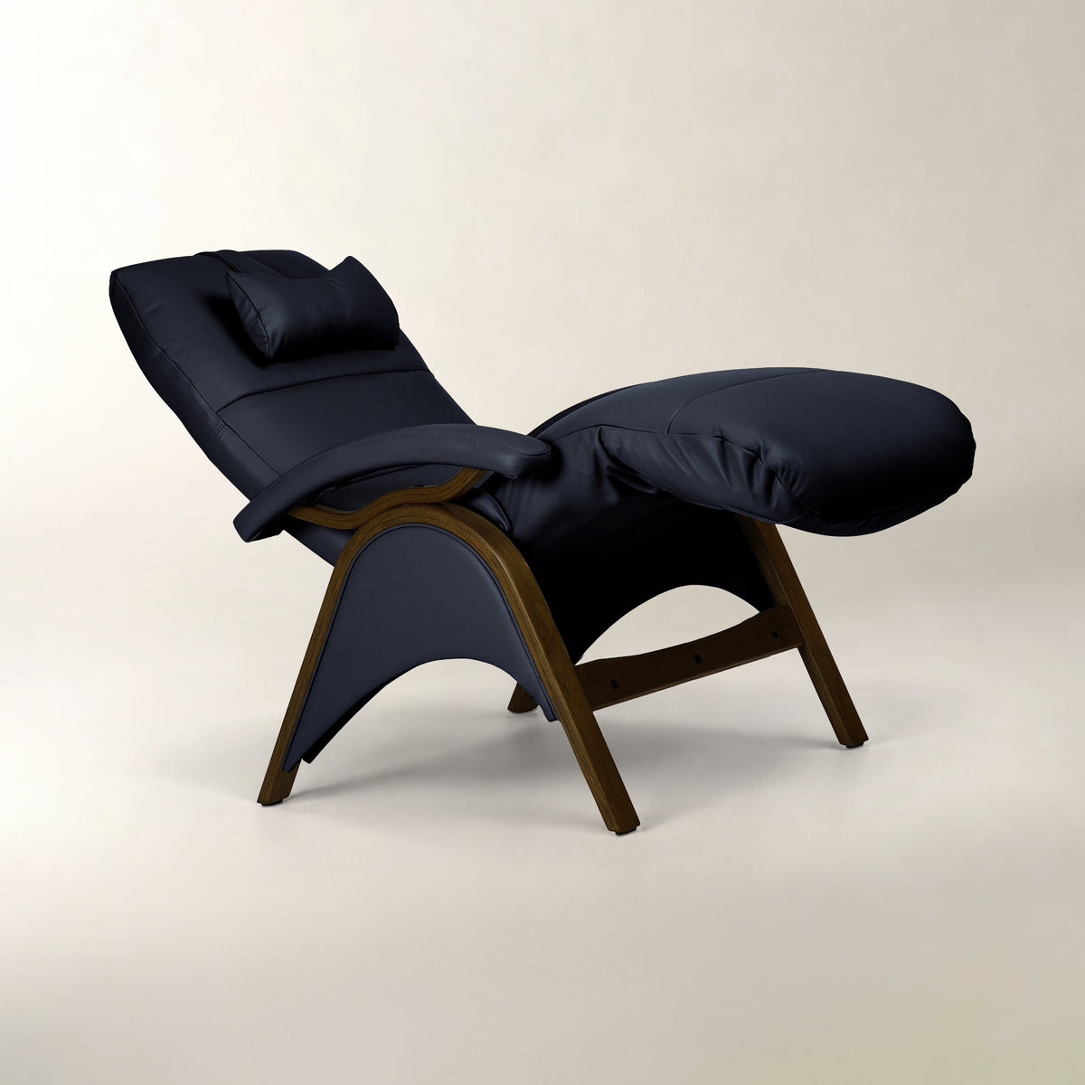 A modern chaise lounge chair with dark navy blue padded fabric upholstery and a curved dark wood frame, shown on a light beige studio background.