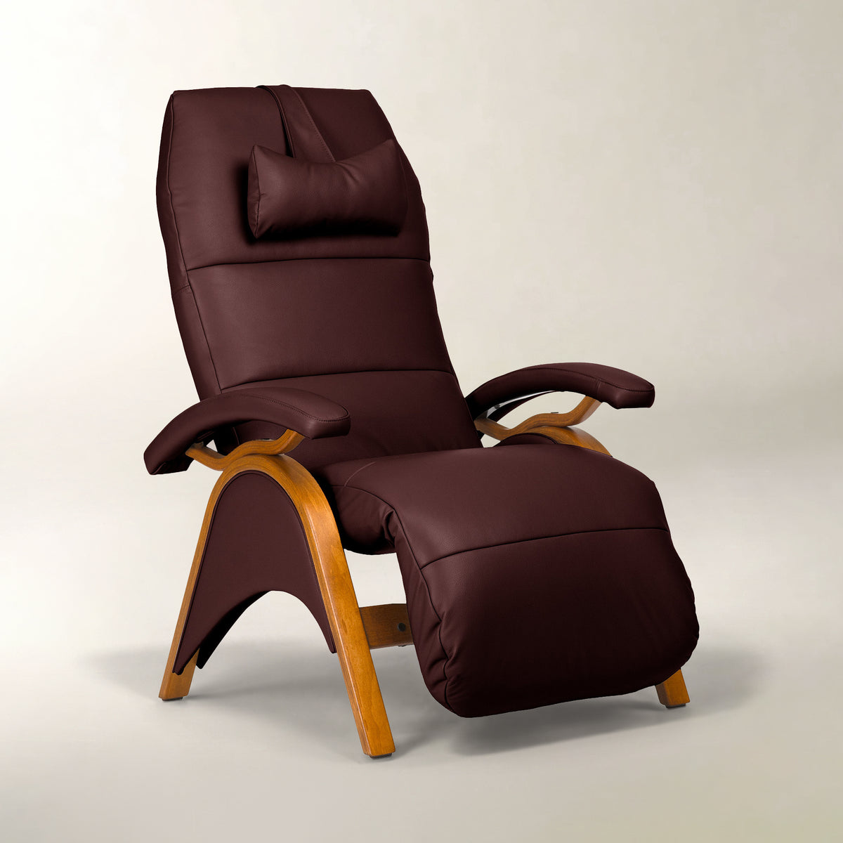 A modern recliner chair upholstered in deep burgundy-brown faux leather with a matching headrest pillow and curved light wood frame, shown on a neutral light gray studio background.