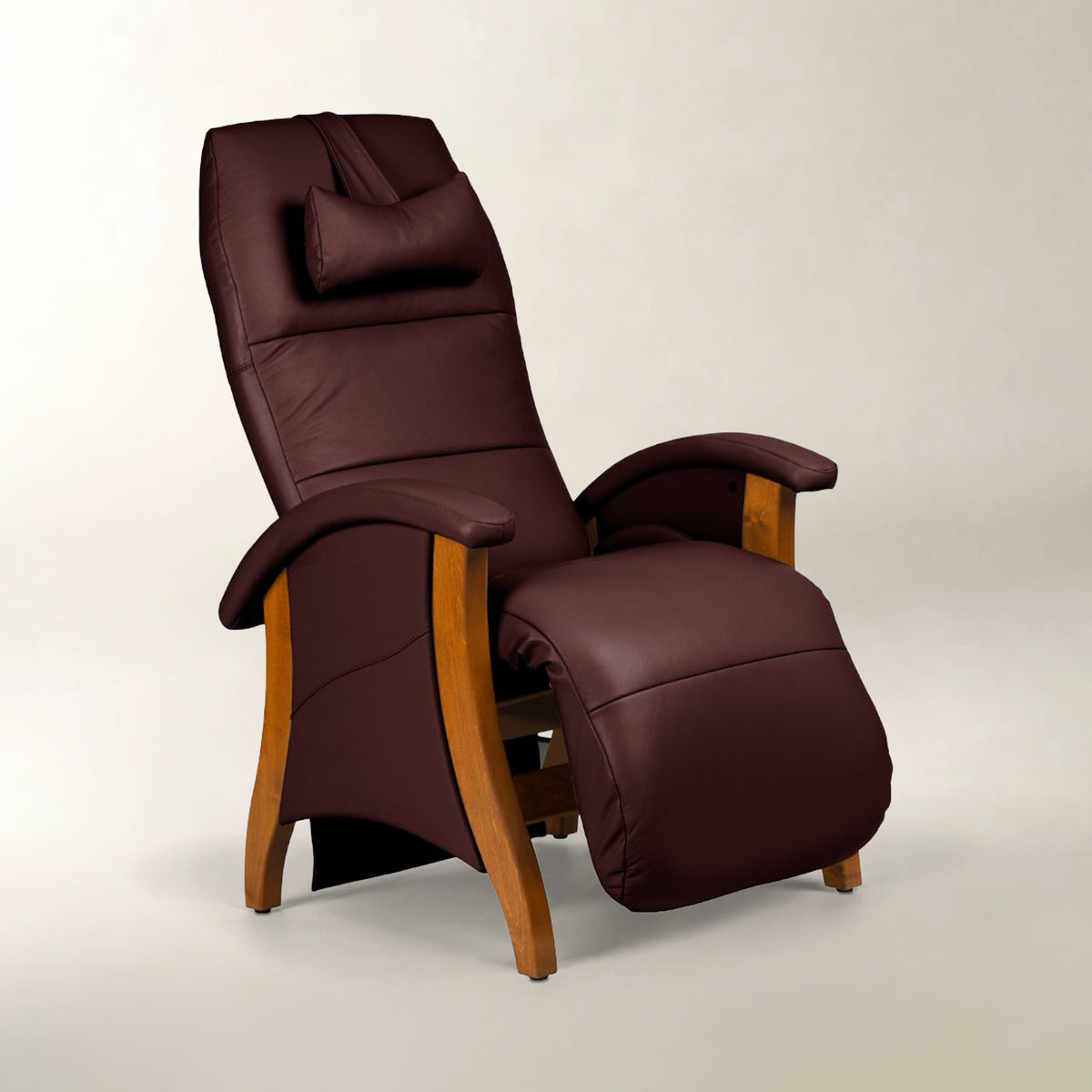 A dark burgundy faux leather recliner chair with a matching headrest pillow and adjustable footrest, featuring light brown wooden legs and arm supports, set against a neutral light gray background.