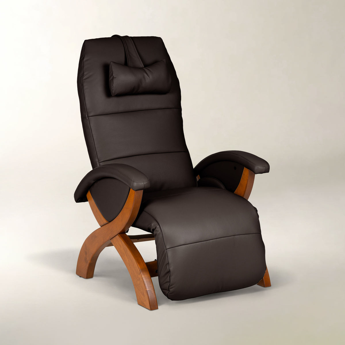 A dark brown faux-leather recliner chair with a matching headrest pillow and curved wooden legs, shown on a neutral light gray background.