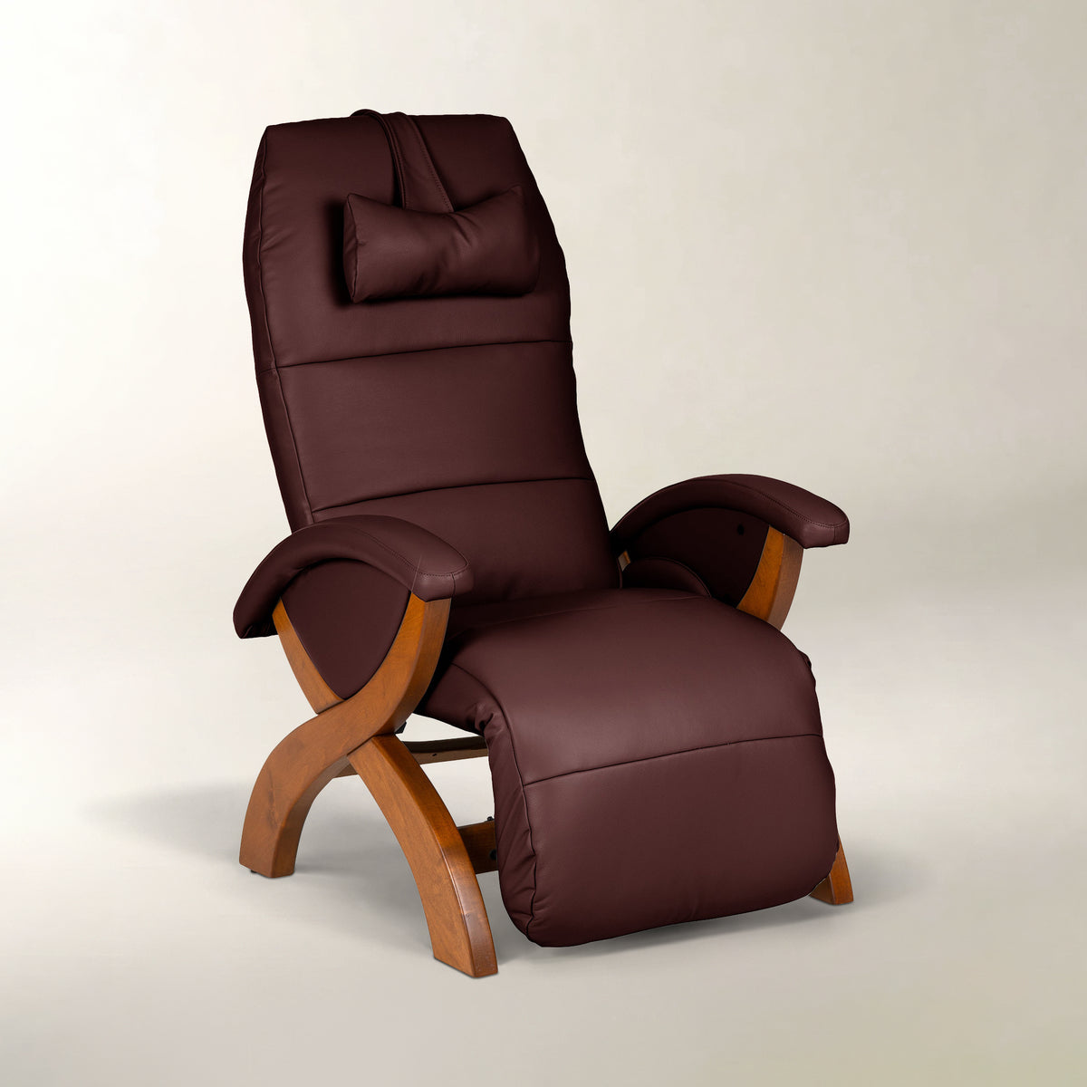 A dark brown faux-leather recliner chair with a matching headrest pillow and curved wooden legs, shown on a neutral light gray background.