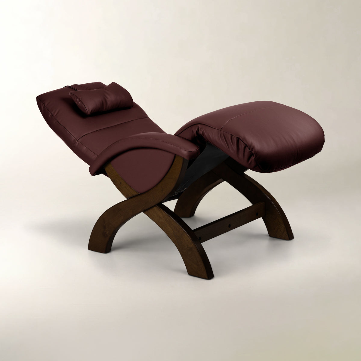A modern lounge chair with a dark brown wooden frame and burgundy leather upholstery, featuring a headrest and an integrated ottoman footrest, set against a plain light beige background.