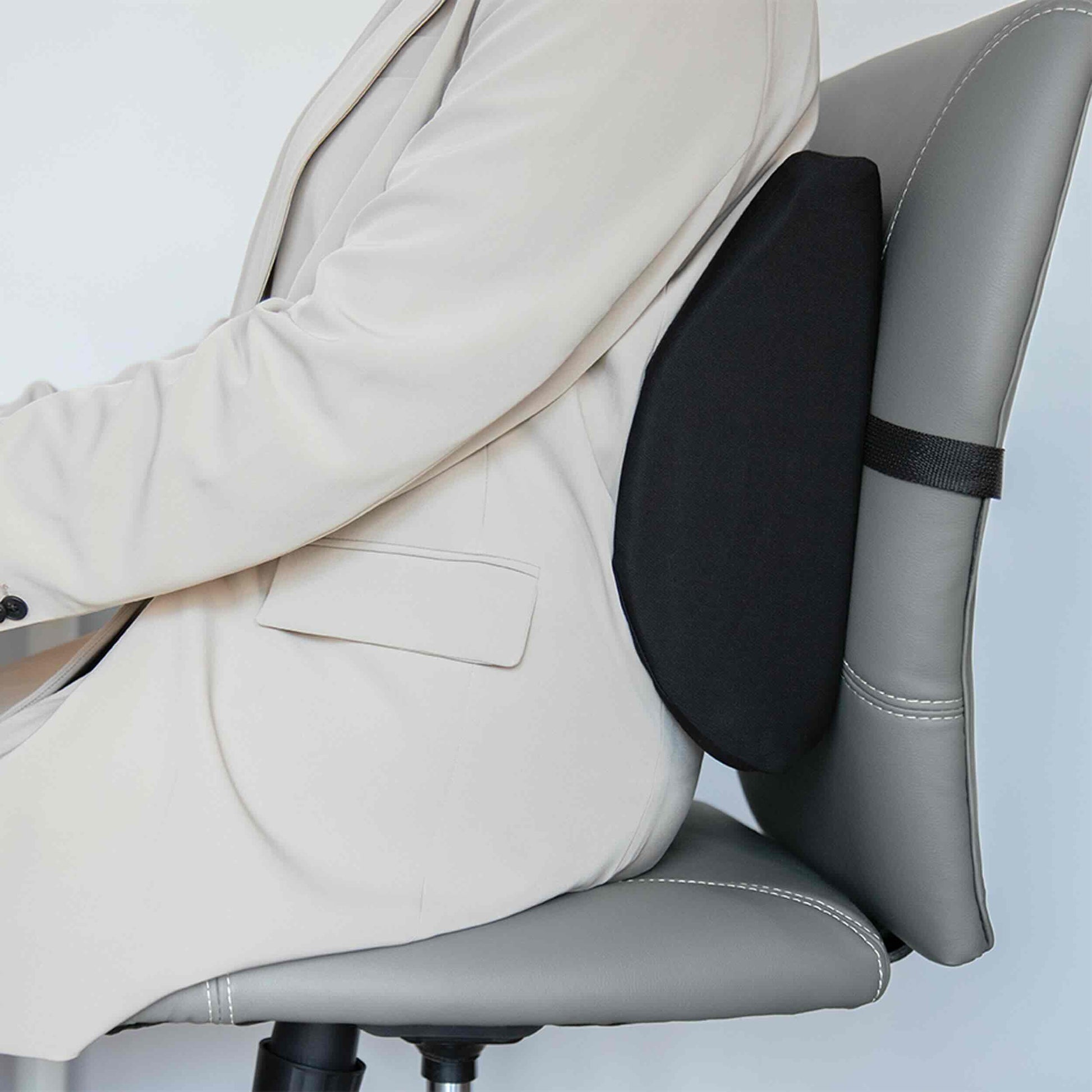 A person in a light beige blazer sits in a gray office chair, demonstrating the use of a black lumbar support cushion attached to the chair's backrest.