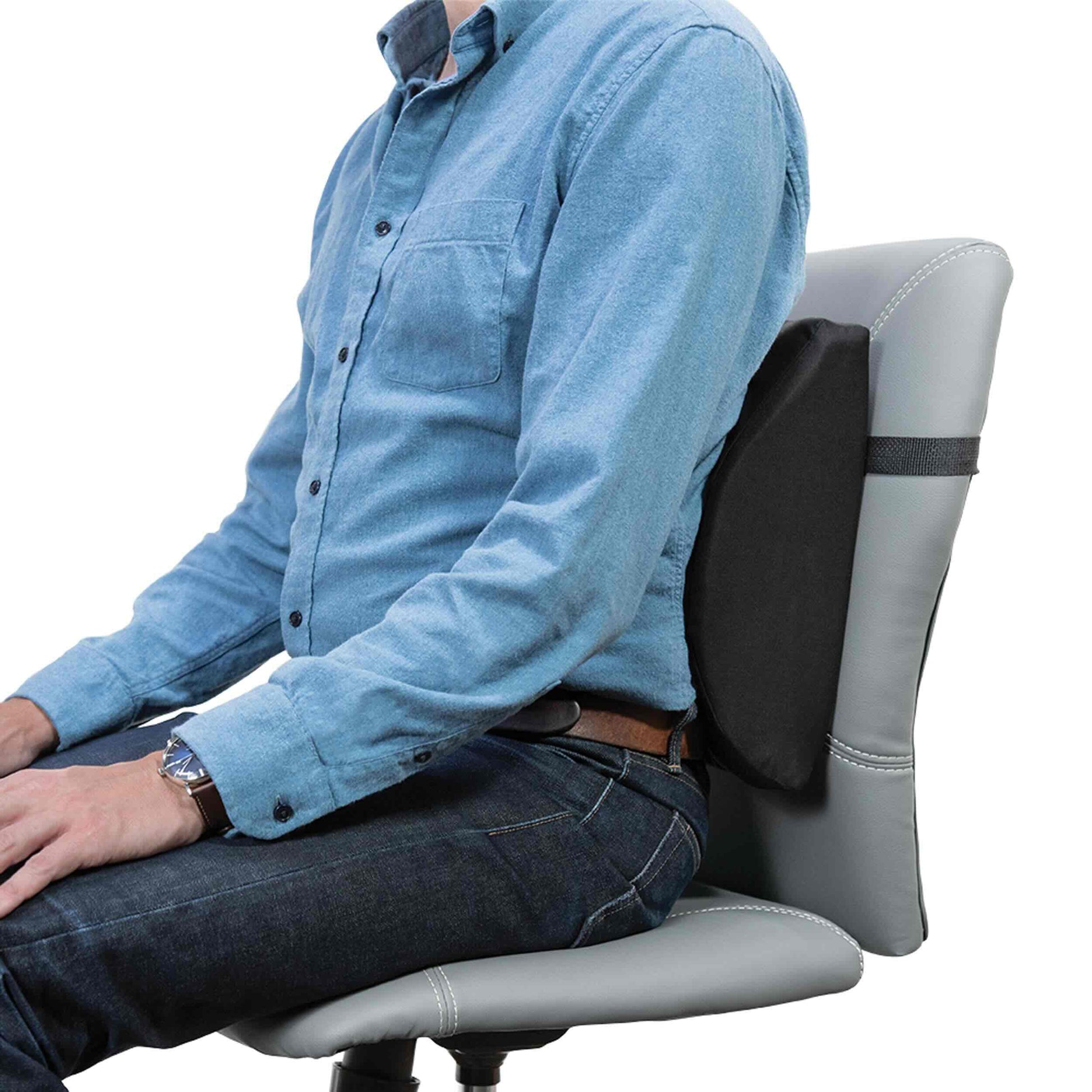 A man wearing a light blue button-down shirt and dark jeans sits on a gray office chair, leaning back against a black lumbar support pad attached to the chair.