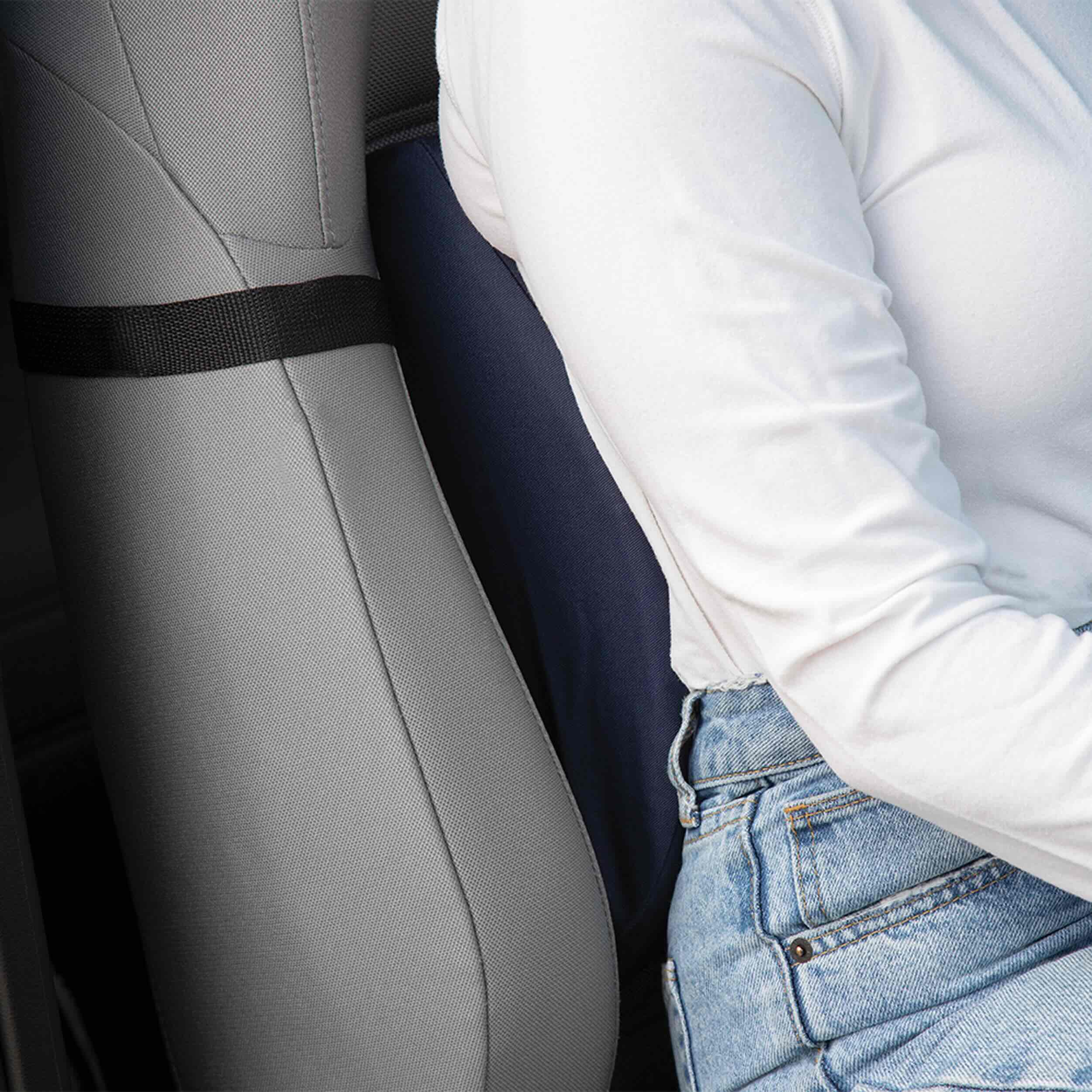A close-up of a gray car seat with a black seat belt strap, next to a person wearing a white long-sleeve top and light blue jeans.