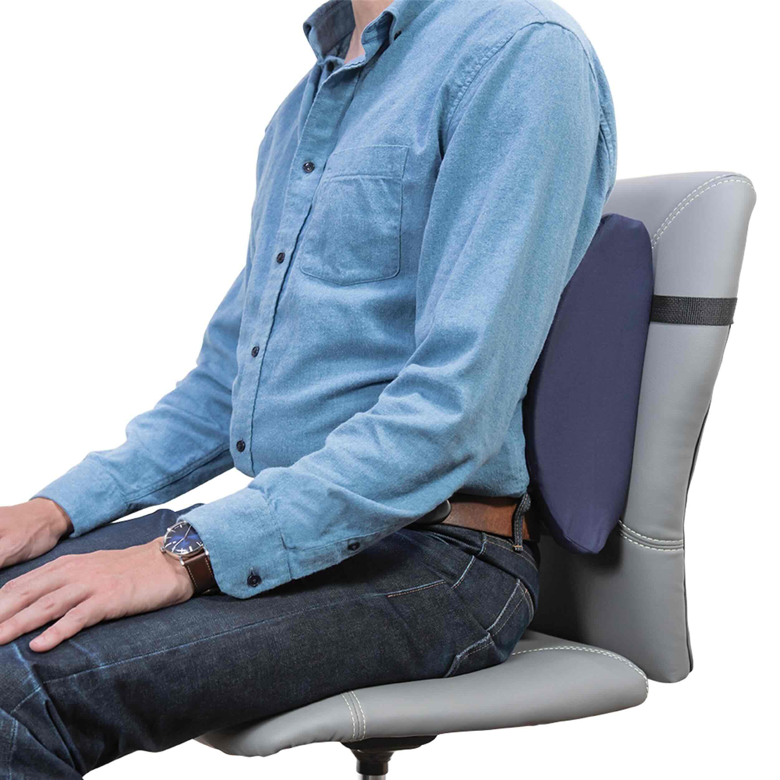A man wearing a light blue button-down shirt and dark jeans sits on a gray office chair, demonstrating a dark blue lumbar support cushion attached to the backrest.
