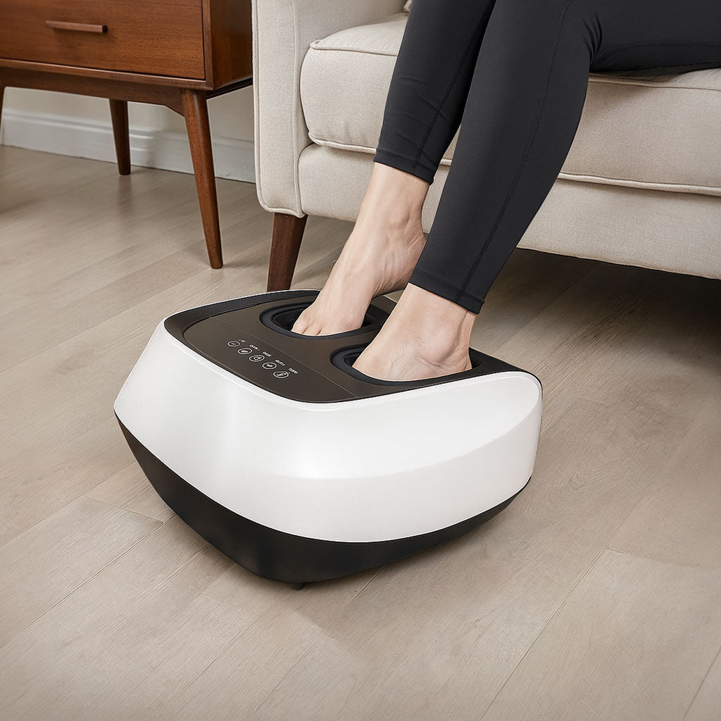 Person using a white and black foot massager on a wooden floor.