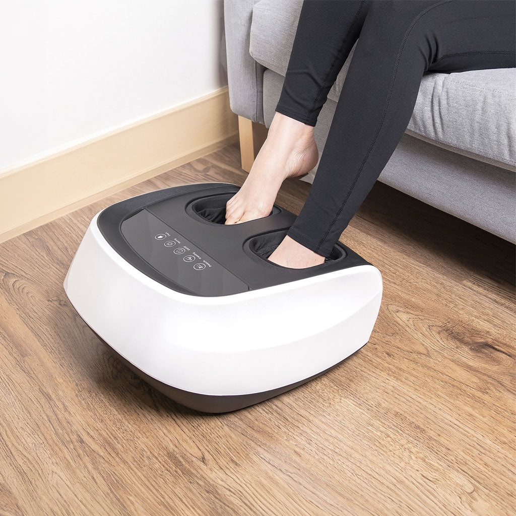 Person using a foot massager on a wooden floor with a couch in the background