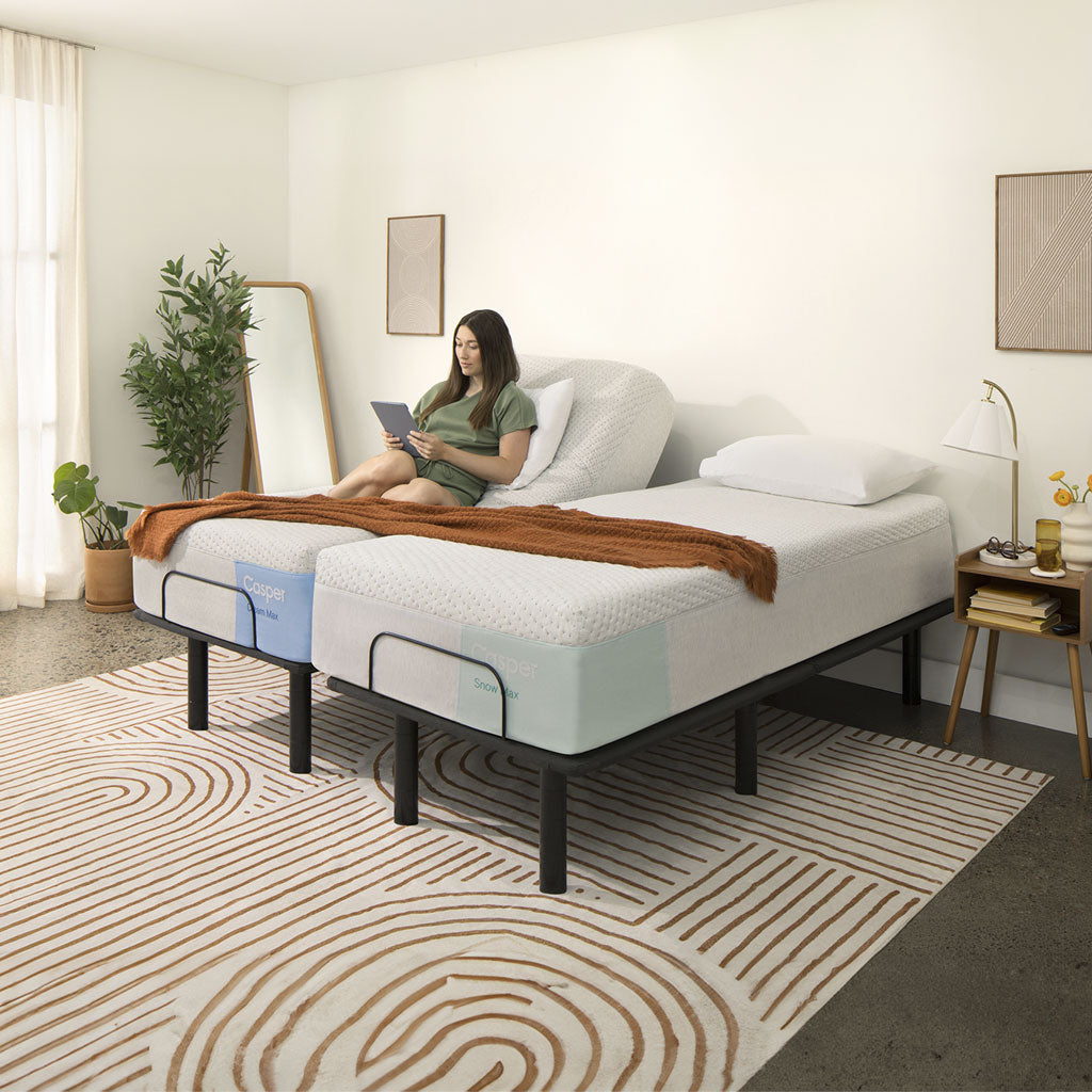 Woman sitting on a bed with a mattress and adjustable base in a bedroom setting.
