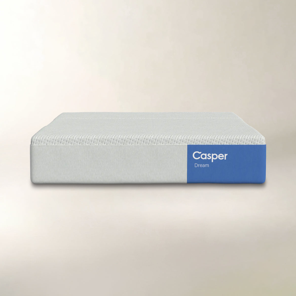 A Casper Dream mattress shown from a front angle against a neutral beige background. The mattress has a light gray textured top and a solid blue side panel with the white Casper brand logo.