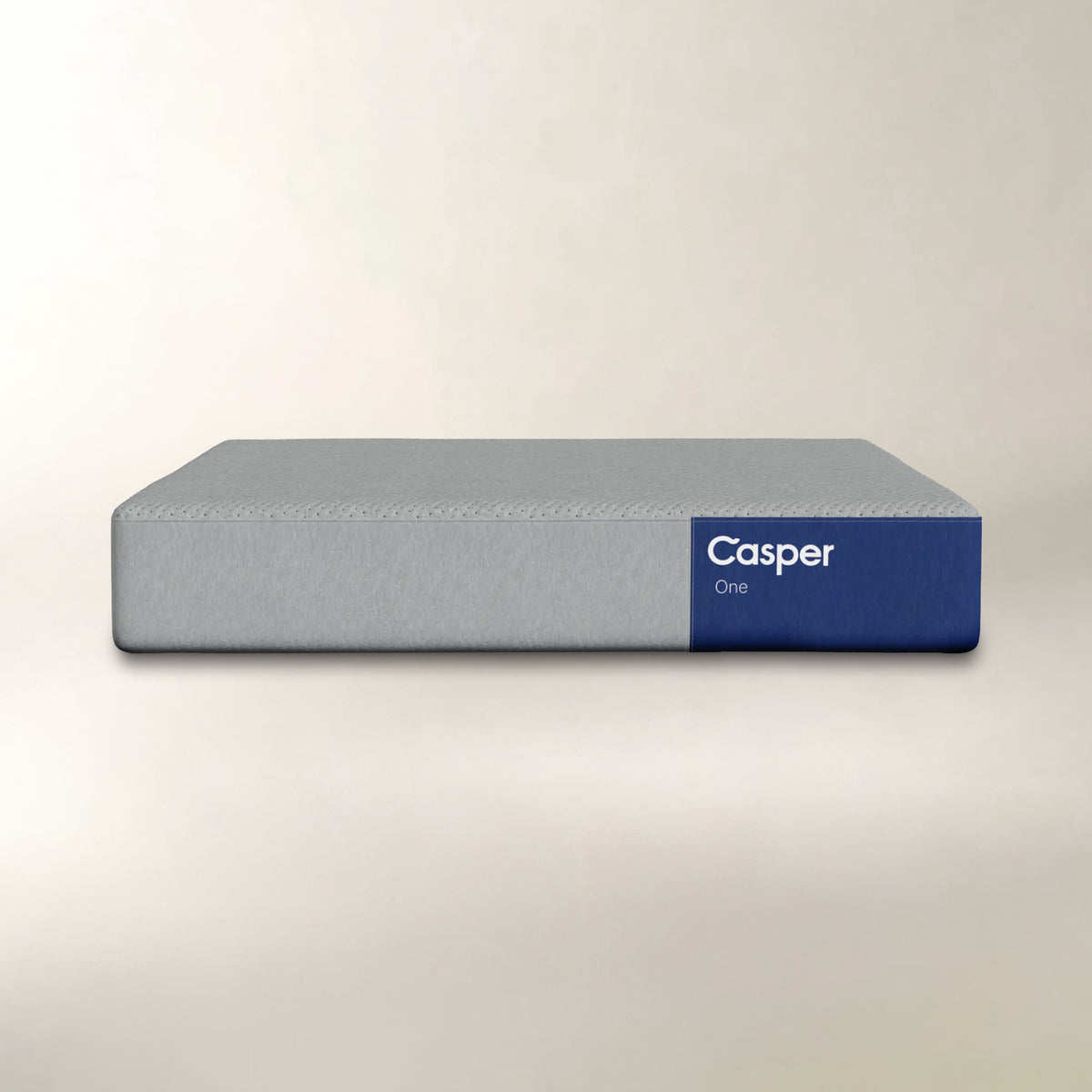 A Casper One mattress shown from a front angle against a neutral, light beige background. The mattress features a textured light gray fabric on the top and side, with a solid dark blue end cap on the right side displaying the white 'Casper One' brand logo.