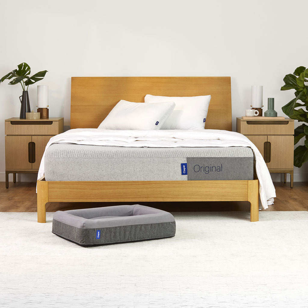 Bed with a mattress labeled 'Original' in a bedroom setting with wooden furniture and plants.