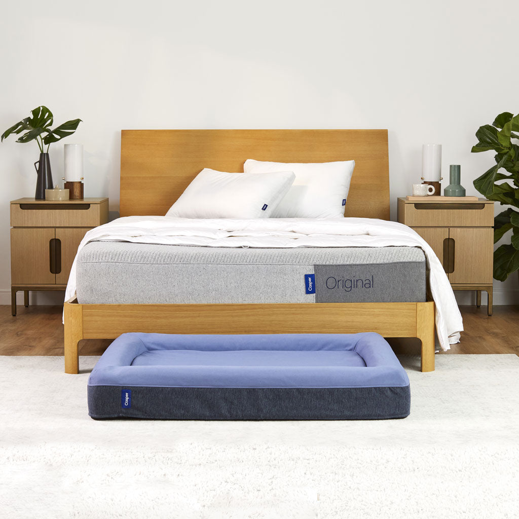 Bed with wooden frame and white bedding, accompanied by a blue pet bed in front.