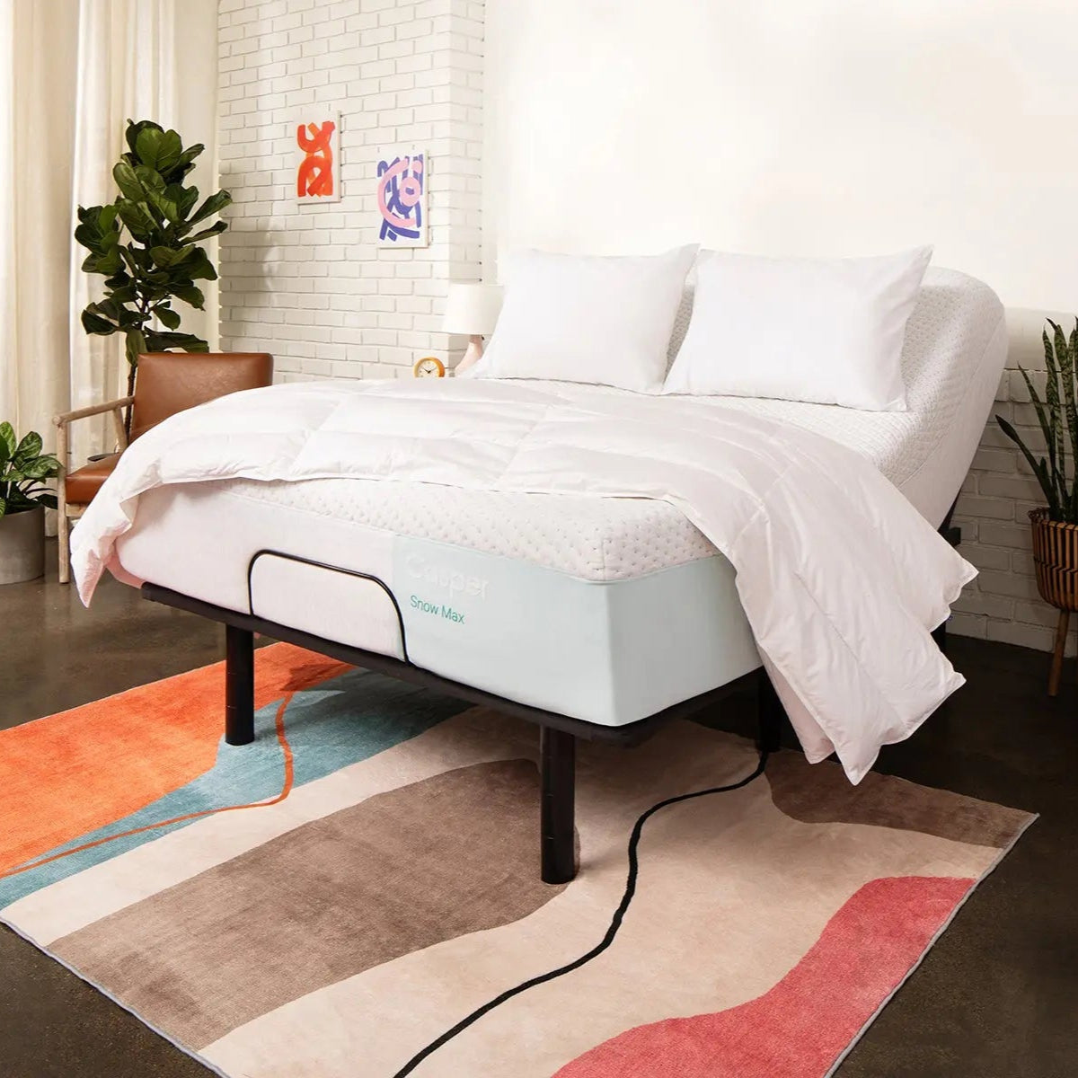 Bed with white bedding and a visible mattress brand logo in a room with a colorful rug and plants.