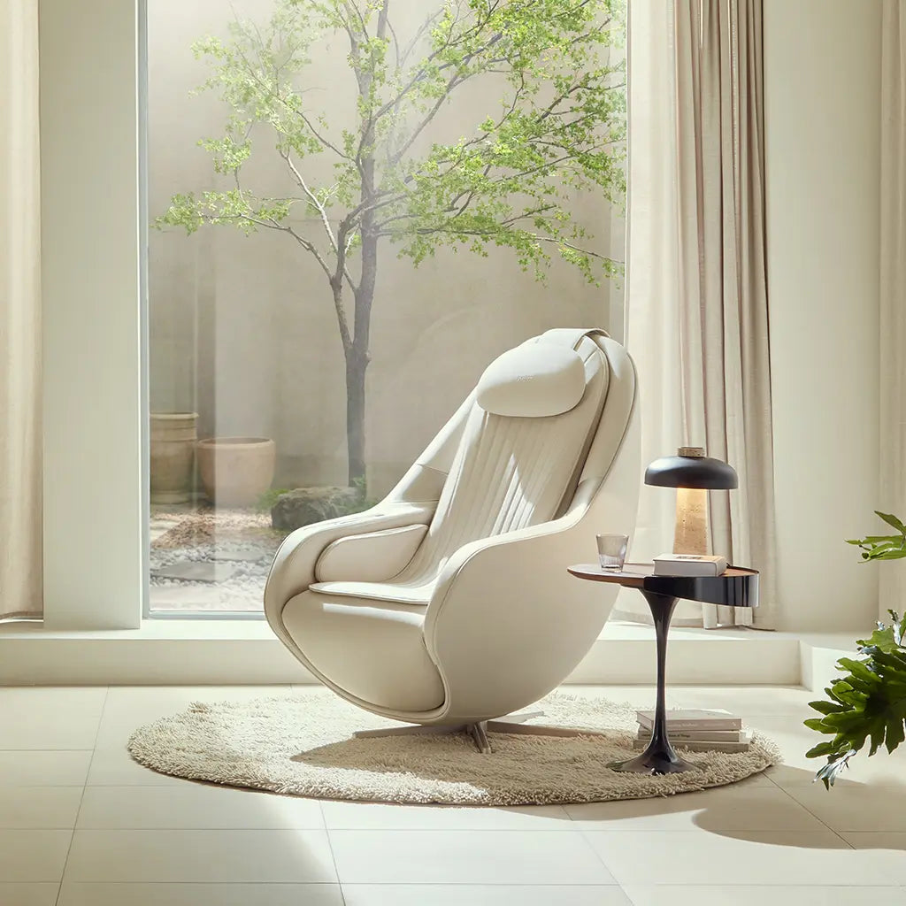 Modern white armchair in a bright room with large windows and a tree outside.