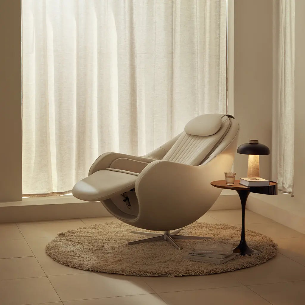 Beige recliner chair in a room with large windows and a small table with a lamp and book.