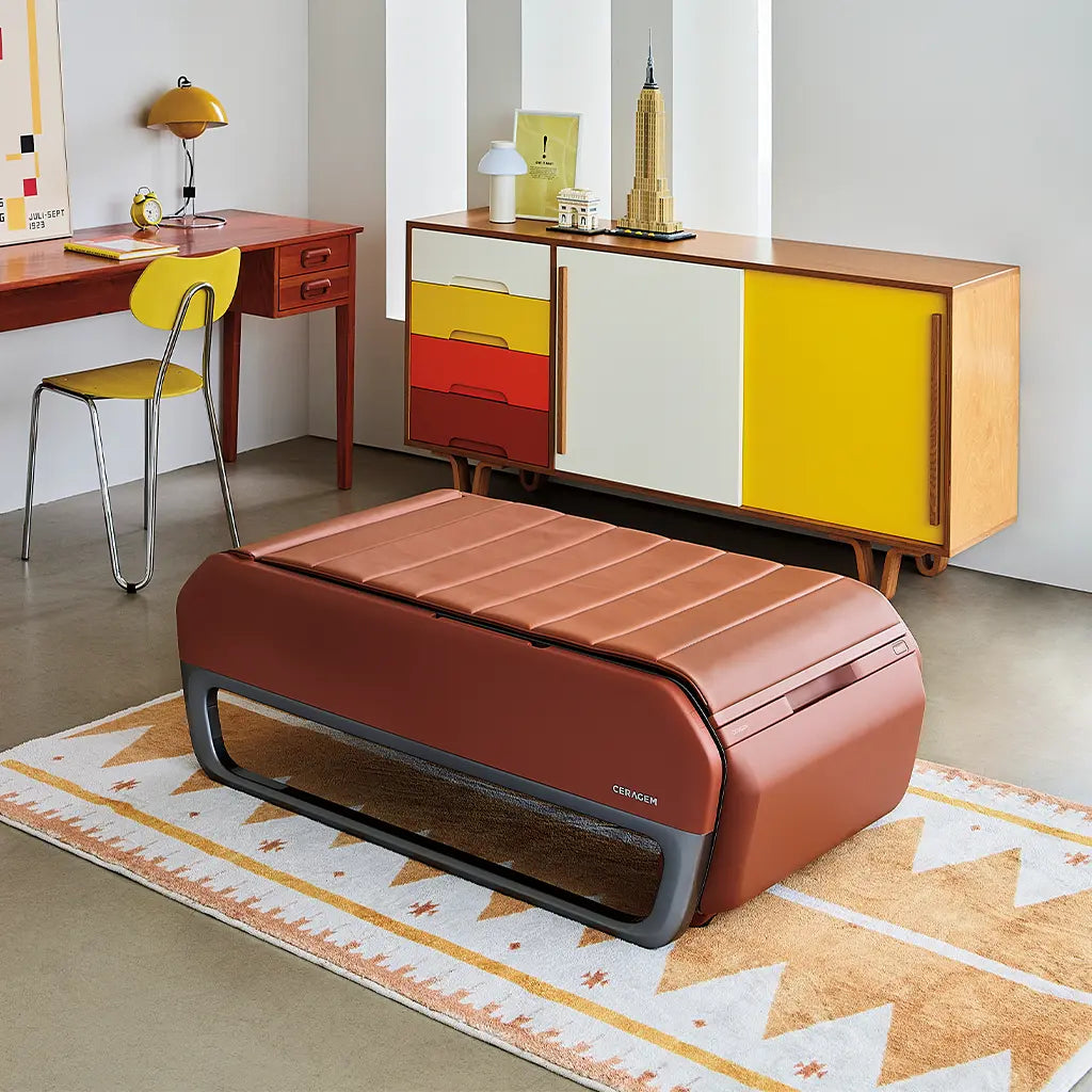 Modern room with a brown massage bed, yellow chair, and colorful sideboard.