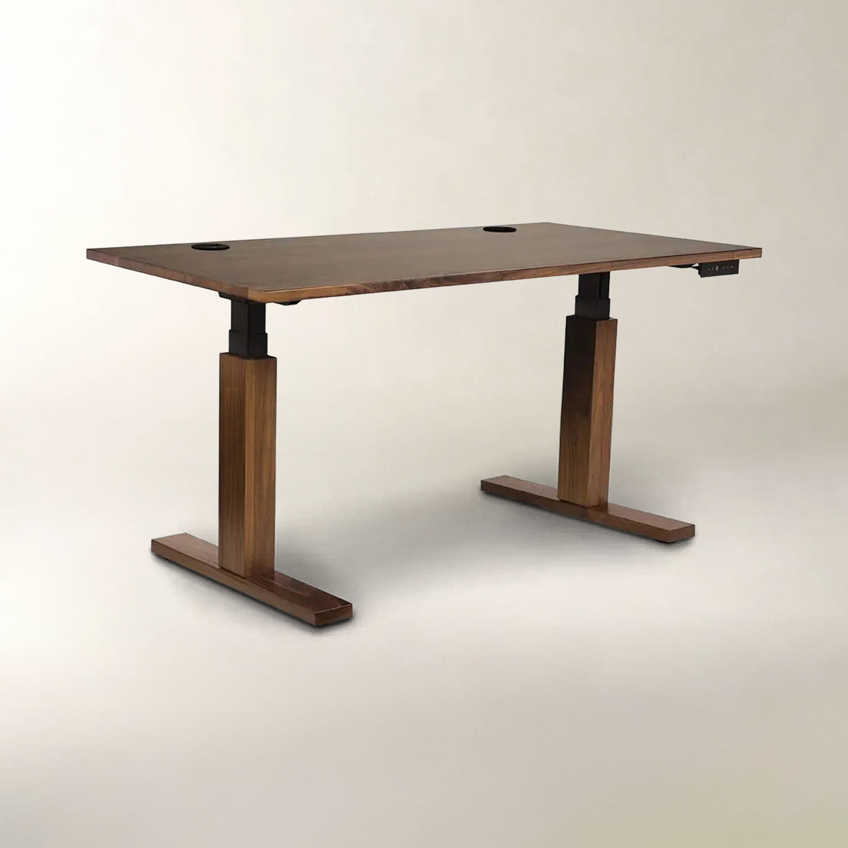 A modern adjustable height standing desk with a dark brown wood grain finish, featuring T-style legs and cable management holes on the top surface, set against a plain light beige background.